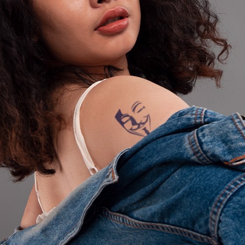 Người phụ nữ mặc áo khoác denim hở vai, để lộ hình xăm mặt nạ trên cánh tay.