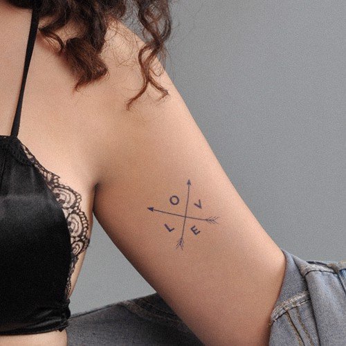 Hình xăm chữ "LOVE" và mũi tên trên cánh tay người mặc áo ren đen và áo khoác jean.