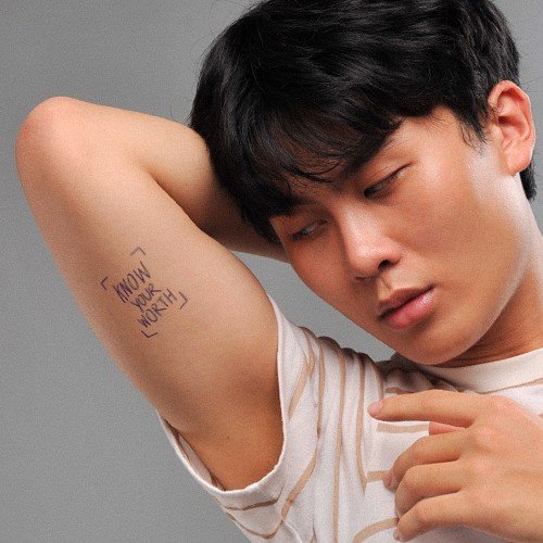 Người đàn ông trong áo thun trắng đang giơ tay, để lộ dòng chữ viết tay trên cánh tay.