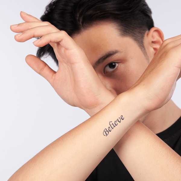 believe_1_324193df48db45b697890cd17c3b288c_grande Người giơ tay chữ X trước mặt, trên cổ tay có hình xăm chữ "Believe".