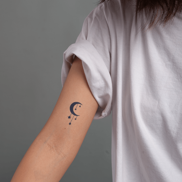 Cánh tay với hình xăm mặt trăng và sao, áo thun trắng xắn tay.