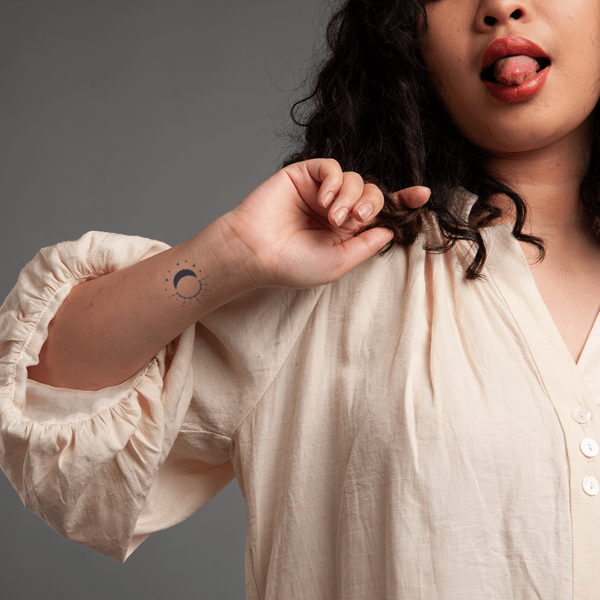 Người mặc áo trắng với hình xăm mặt trăng trên cổ tay, đang đưa lưỡi ra.