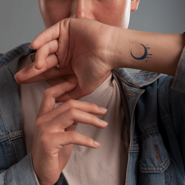 Người mặc áo khoác jean, giơ tay có hình xăm mặt trăng, che một phần khuôn mặt.