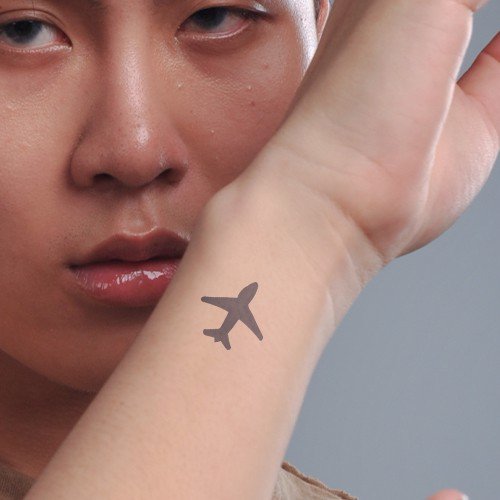 Một người giơ cổ tay có hình xăm máy bay nhỏ màu đen, khuôn mặt nhìn thẳng vào ống kính.