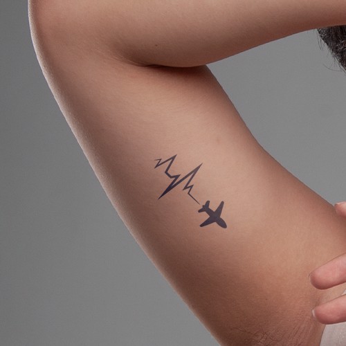 Hình xăm hình máy bay và đường nhịp tim trên cánh tay một người, nền xám.