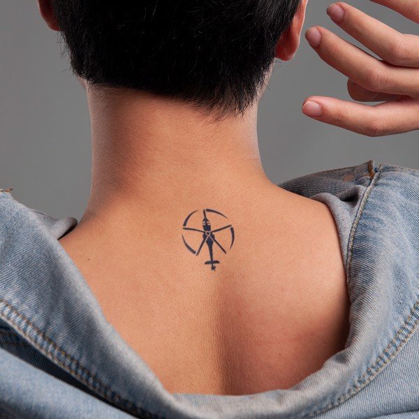 Hình xăm nhỏ hình cung thủ trên cổ một người, áo khoác denim kéo xuống, tay chạm nhẹ vào cổ.